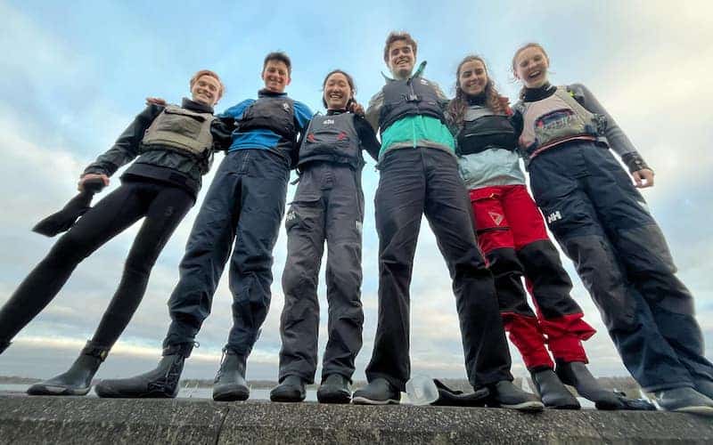 Cambridge sailors standing on a wall in their sailing kit